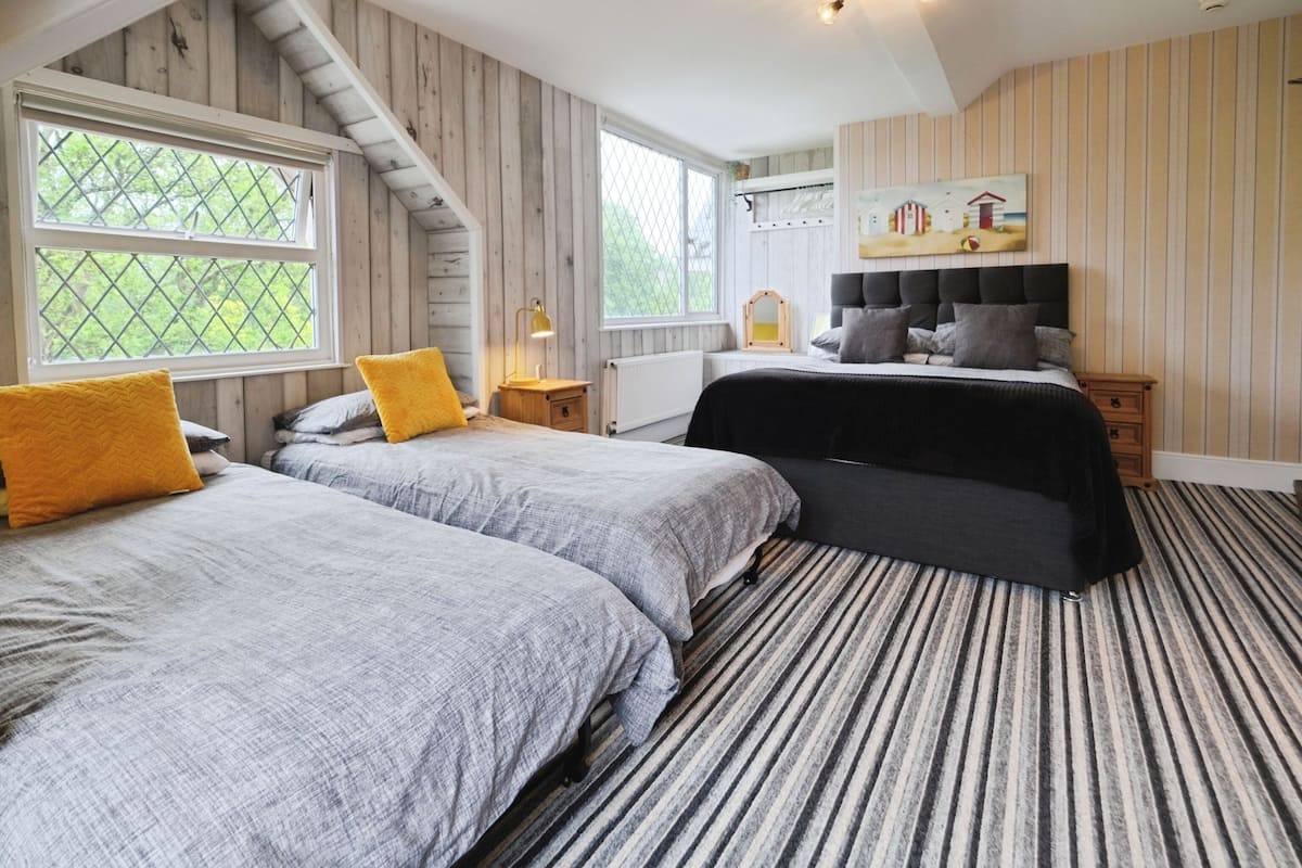 A bedroom with two beds, a large window, a radiator, and a painting on the wall.