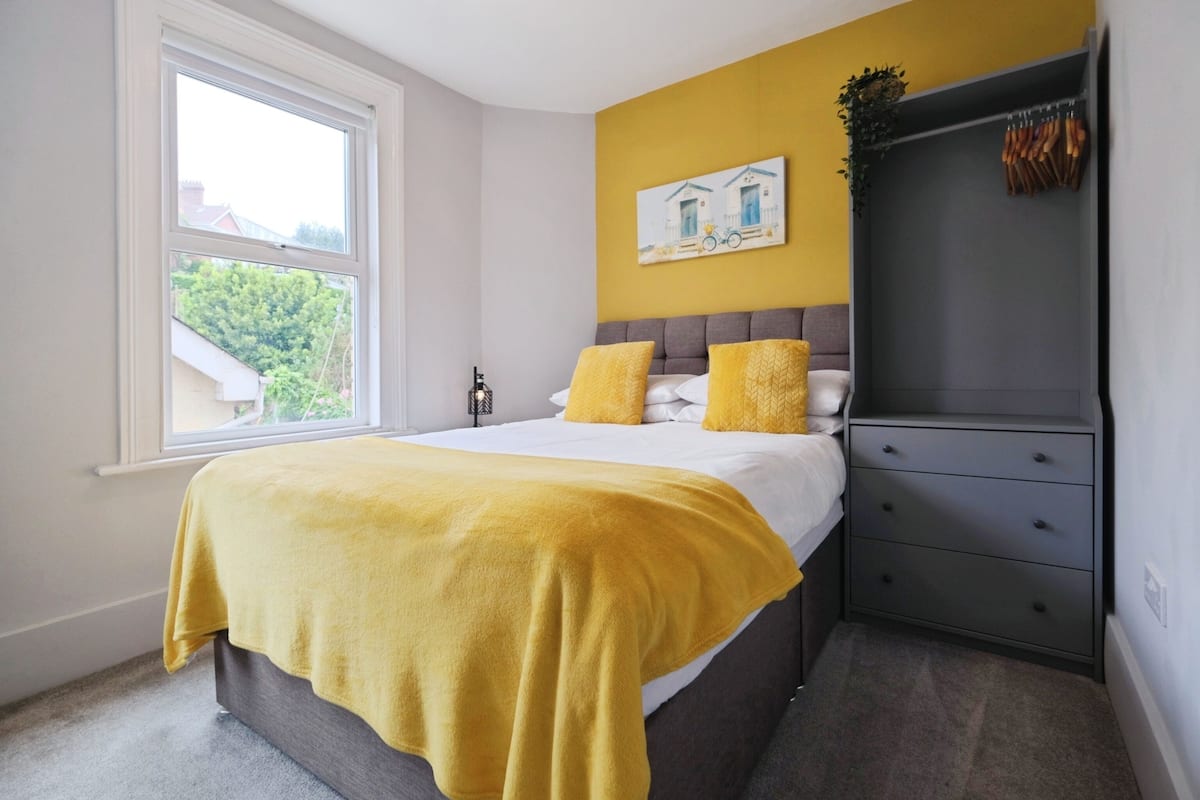 A bedroom with a bed, a window, a dresser, and a painting on the wall.