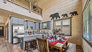 A spacious kitchen with a central island, wooden dining table with chairs, and a balcony with a railing.