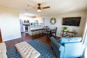 A modern living room with a sofa, ottoman, and a dining area with chairs and a table.