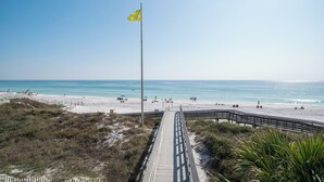 A beach with a wooden boardwalk leading to the shore, a flagpole with a flag, and a clear blue sky. - Gulf View! Pool, Tennis Court, Beach Access (Santa Rosa Beach)
