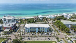 A coastal hotel with a parking lot, palm trees, and a view of the ocean.