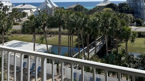 A balcony with a view of a pool, palm trees, and a distant ocean. - Gulf View! Pool, Tennis Court, Beach Access (Santa Rosa Beach)