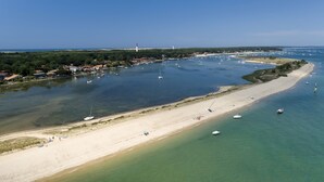 Vue aérienne d’une zone côtière avec une plage de sable, des bateaux et un phare au loin.