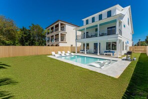 Uma casa de dois andares com piscina, cerca de madeira e gramado bem cuidado.