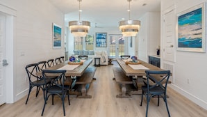 A dining area with a long wooden table, black chairs, and two hanging pendant lights. - Mariner: New! Private Beach! (Miramar Beach)