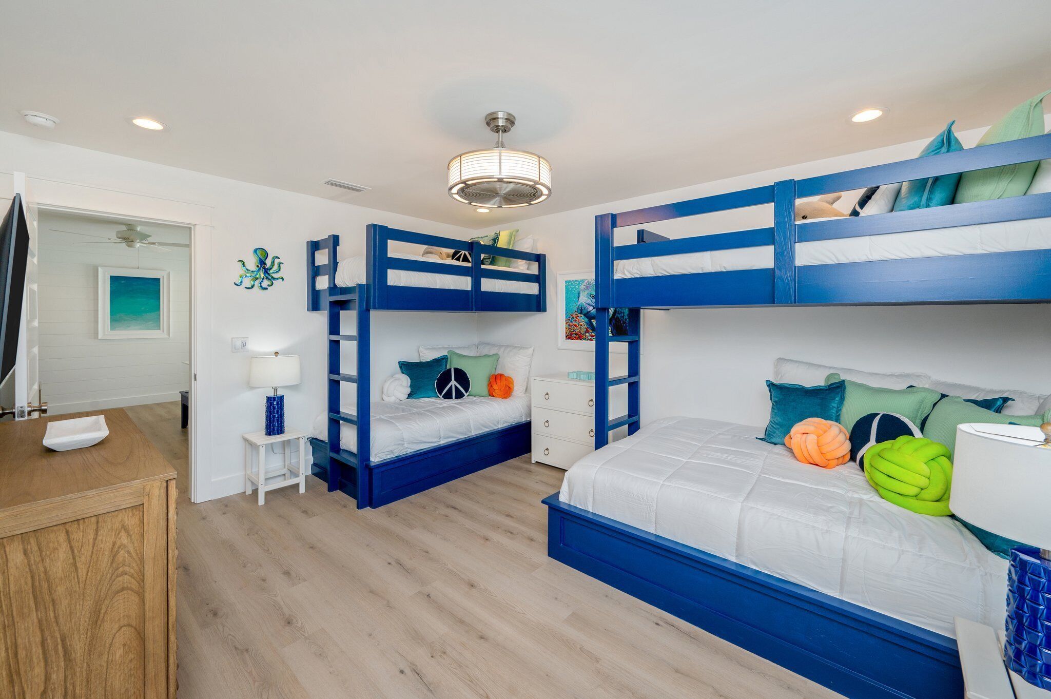 Dormitorio con literas, un escritorio de madera, una mesita con lámpara y un ventilador de techo.