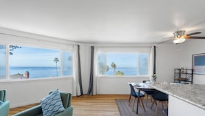 A modern kitchen with large windows, wooden flooring, and a dining area with chairs and a table. - Ocean Front Across From Beach/Amazing Views (La Jolla)