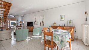 Un amplio salón con una mesa de comedor dispuesta para cuatro personas, un sofá, un televisor y obras de arte en las paredes.