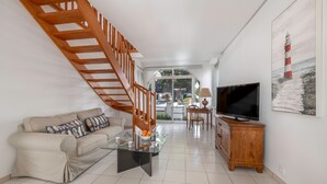 Una sala de estar moderna con una escalera de madera, un sofá, una mesa de centro de vidrio, un televisor y un cuadro de un faro.