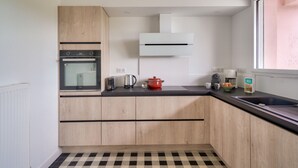 Eine kompakte Küche mit einbauendem Backofen, einem Toaster, einem Wasserkocher und einem roten Topf auf der Arbeitsfläche.