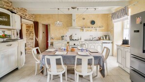 Une cuisine spacieuse avec des meubles blancs, une table à manger pour quatre personnes et un grand réfrigérateur.