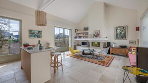 A spacious living area with a large window, a central island with stools, a TV, and a bookshelf. - Renovated house for 7 with garden, near beach (Batz-sur-Mer)