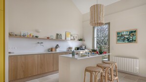 A modern kitchen with a central island, wooden cabinetry, and a hanging light fixture. - Renovated house for 7 with garden, near beach (Batz-sur-Mer)