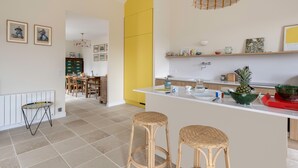 A modern kitchen with a central island, bar stools, and a dining area with chairs and a table. - Renovated house for 7 with garden, near beach (Batz-sur-Mer)