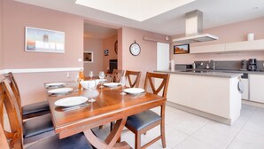 A modern kitchen with a dining area, featuring a wooden dining table set for four, a kitchen island, and a skylight above. - House for 8 – Les Sables – 950m from beach (Les Sables-d´Olonne)