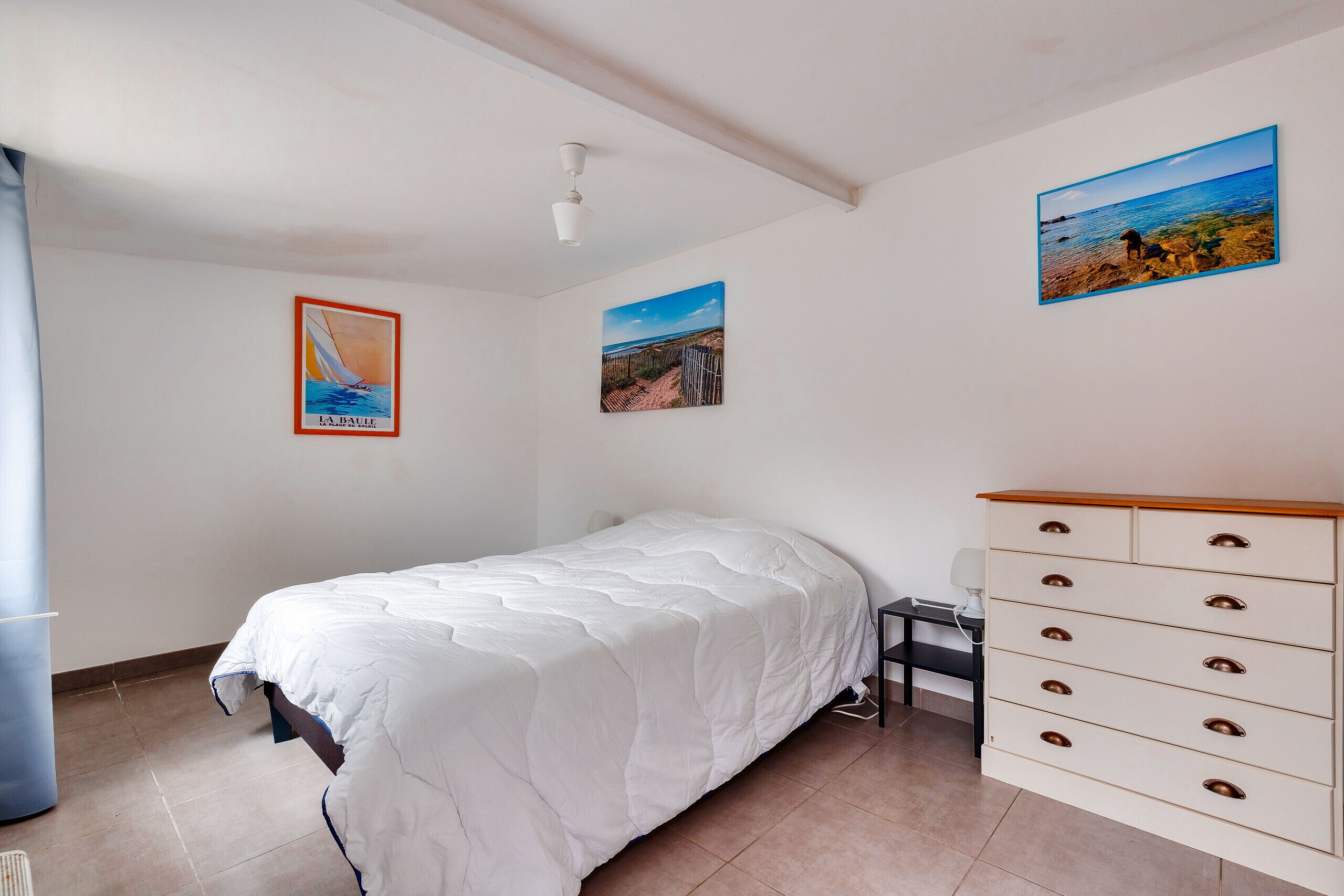 A bedroom with a bed, a dresser, and two wall-mounted pictures.