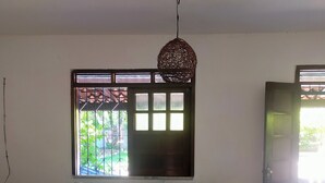 A room with a wooden sofa, a hanging light fixture, a window with bars, and a door. - Cozy vacation home surrounded by greenery a few steps from the sea (Itaparica)