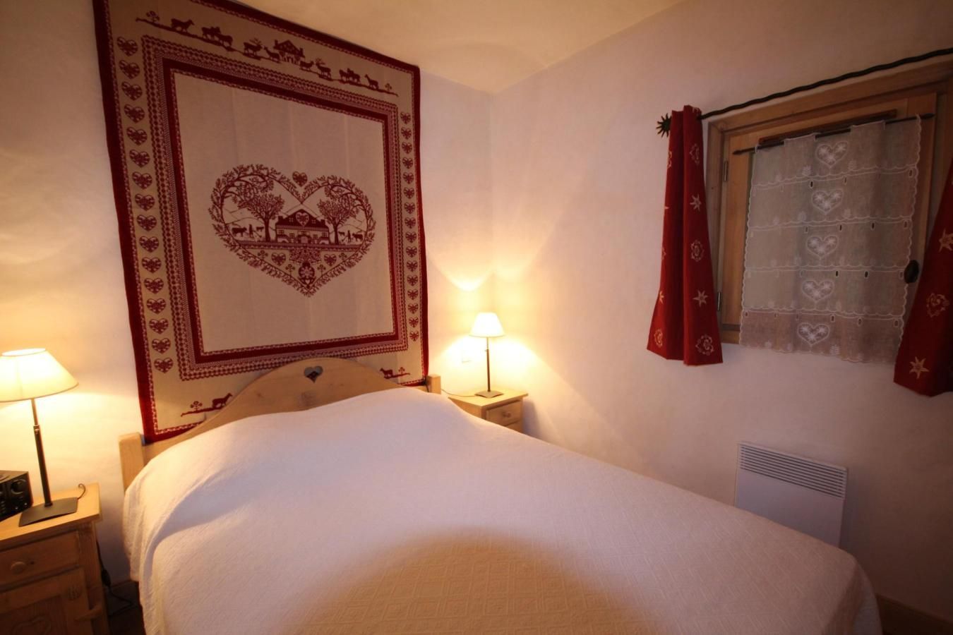 Ein Hotelzimmer mit einem Bett, zwei Nachttischlampen, einer Wandteppich, einem Fenster mit Vorhängen und einer Heizung.
