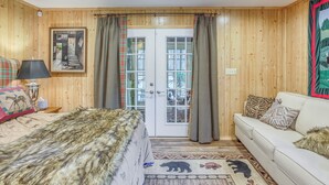 A wooden-paneled room with a bed, a white sofa, a lamp, and a framed picture on the wall. - Tranquil Fairmont Studio w/ Patios - Pets Welcome! (Fairmont)