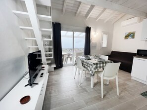 A modern kitchen with white cabinetry, a dining area with a checkered tablecloth, and a view through a glass door to the outside. - Affittimoderni Castelsardo The Sun - CSSO12 (Castelsardo)