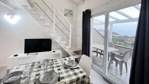 Ein Essbereich mit kariertem Tischläufer, weißen Stühlen und einer Treppe, die zu einem Balkon mit Aussicht führt.