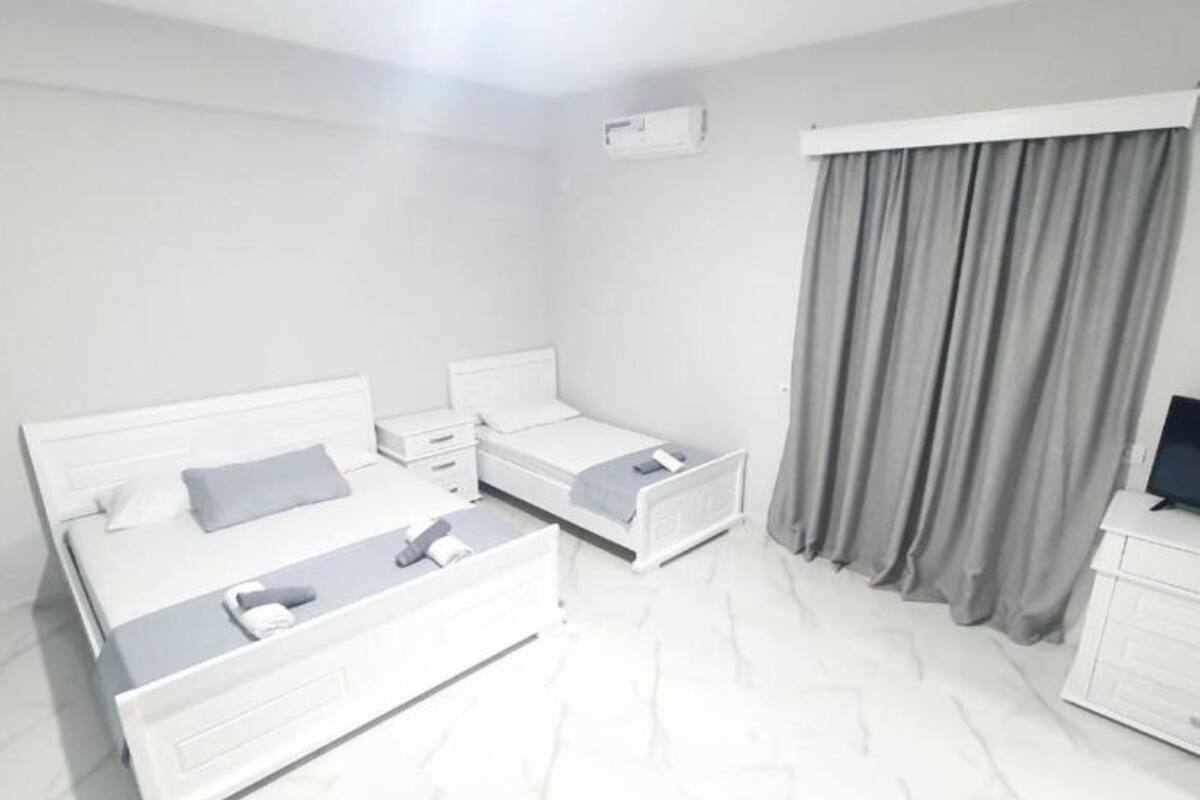 A modern hotel room with a large bed, a smaller bed, a desk, and a TV.