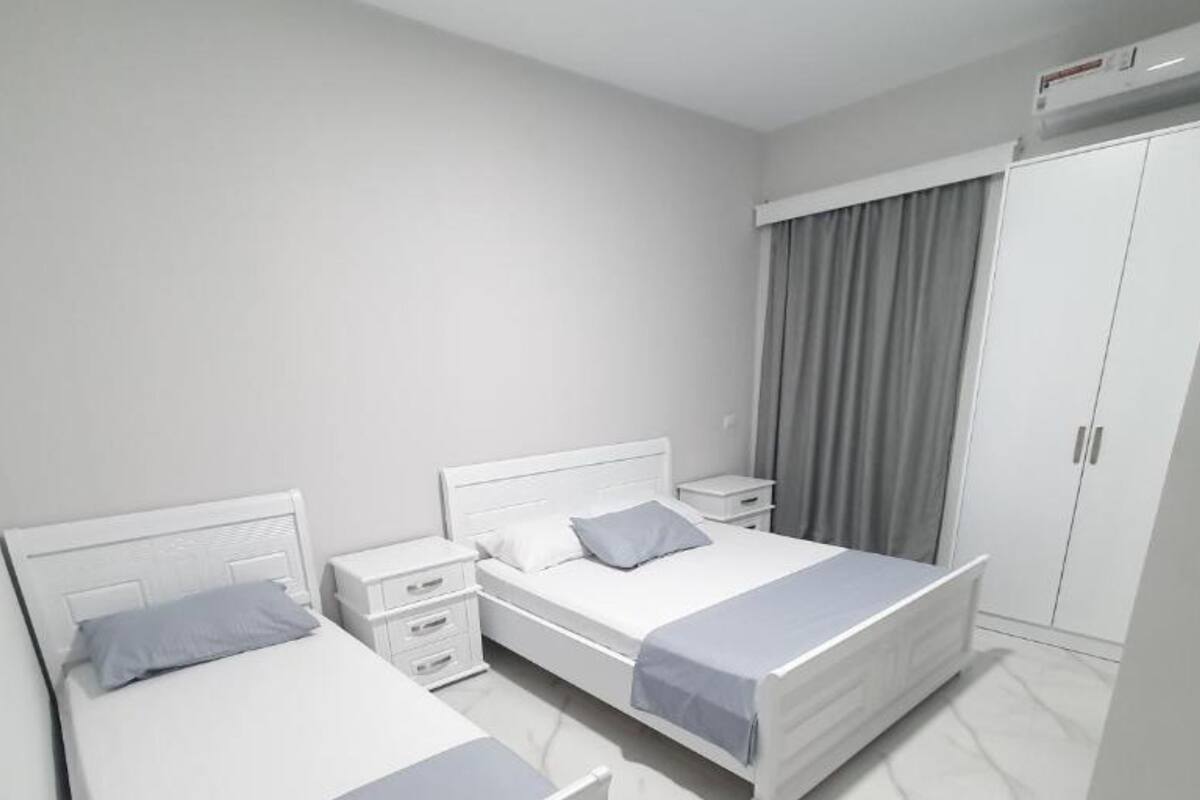 A modern bedroom with two single beds, a nightstand, a wardrobe, and a window with curtains.