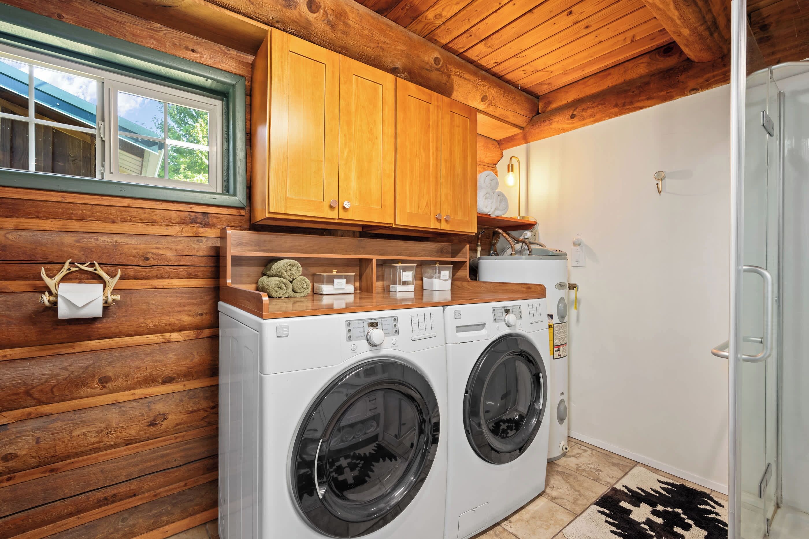A laundry area with a washing machine and dryer, wooden cabinets, a window, and a towel rack.