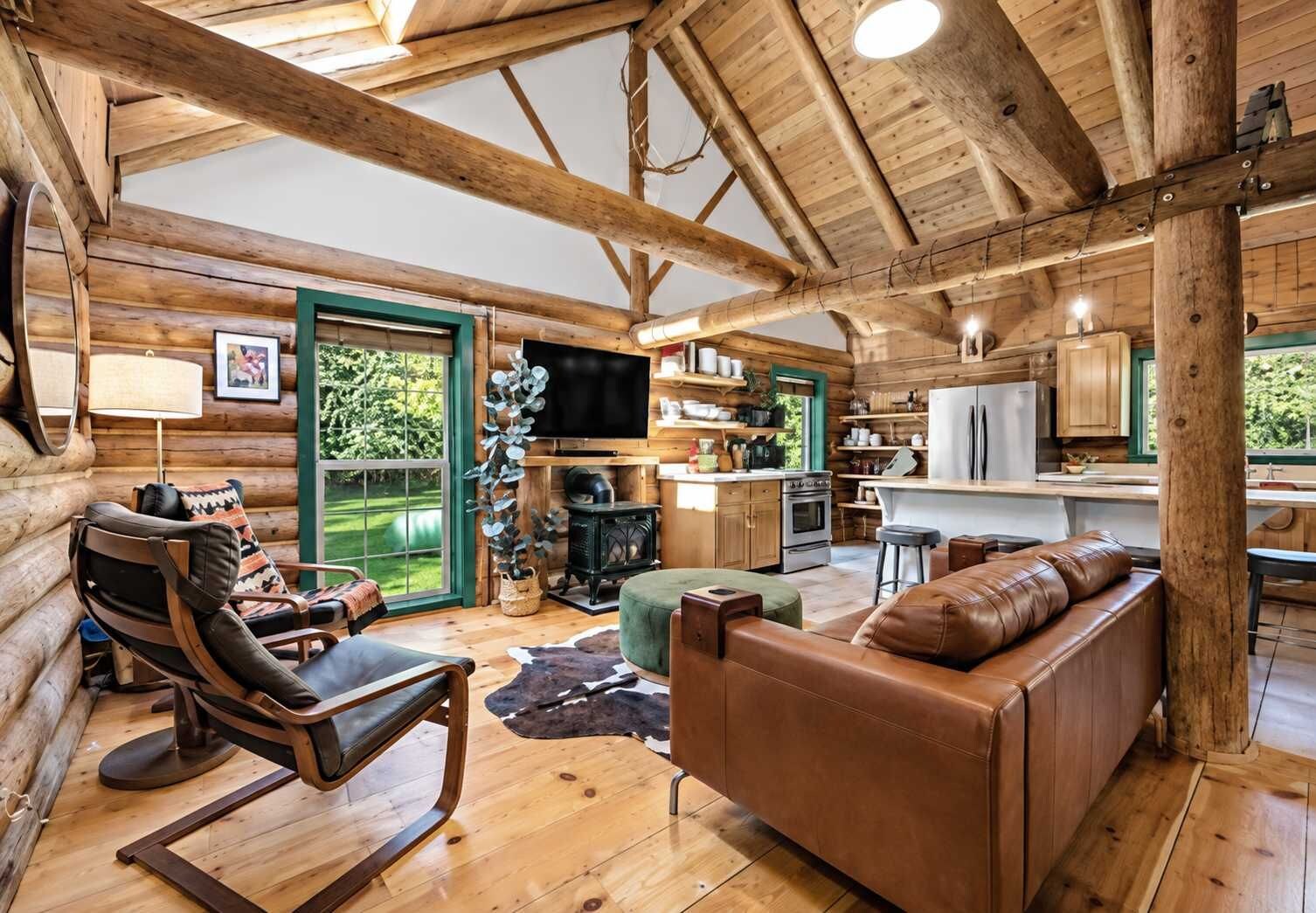 A log cabin interior with a fireplace, leather furniture, and a kitchen area.