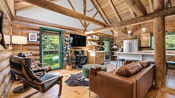 A log cabin interior with a fireplace, leather furniture, and a kitchen area.