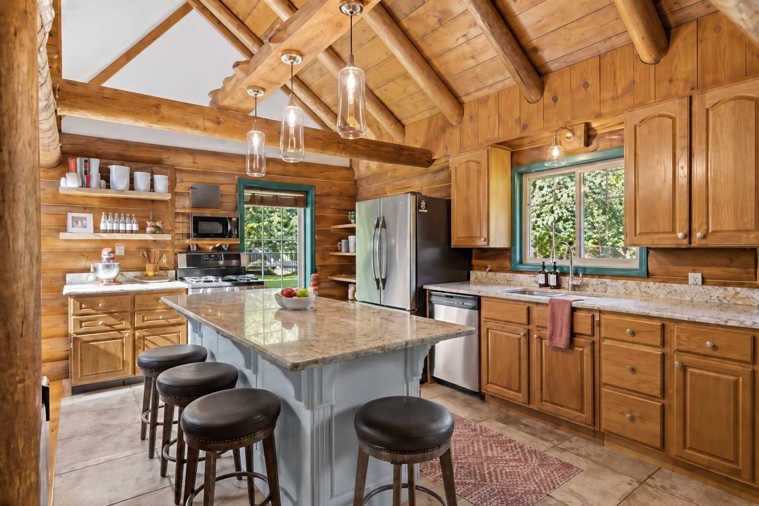 A spacious kitchen with wooden cabinets, a central island with stools, and a view of greenery outside.