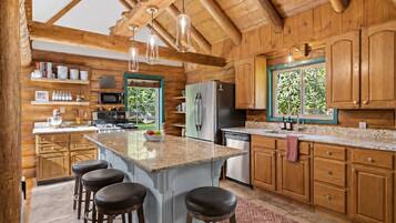 A spacious kitchen with wooden cabinets, a central island with stools, and a view of greenery outside.