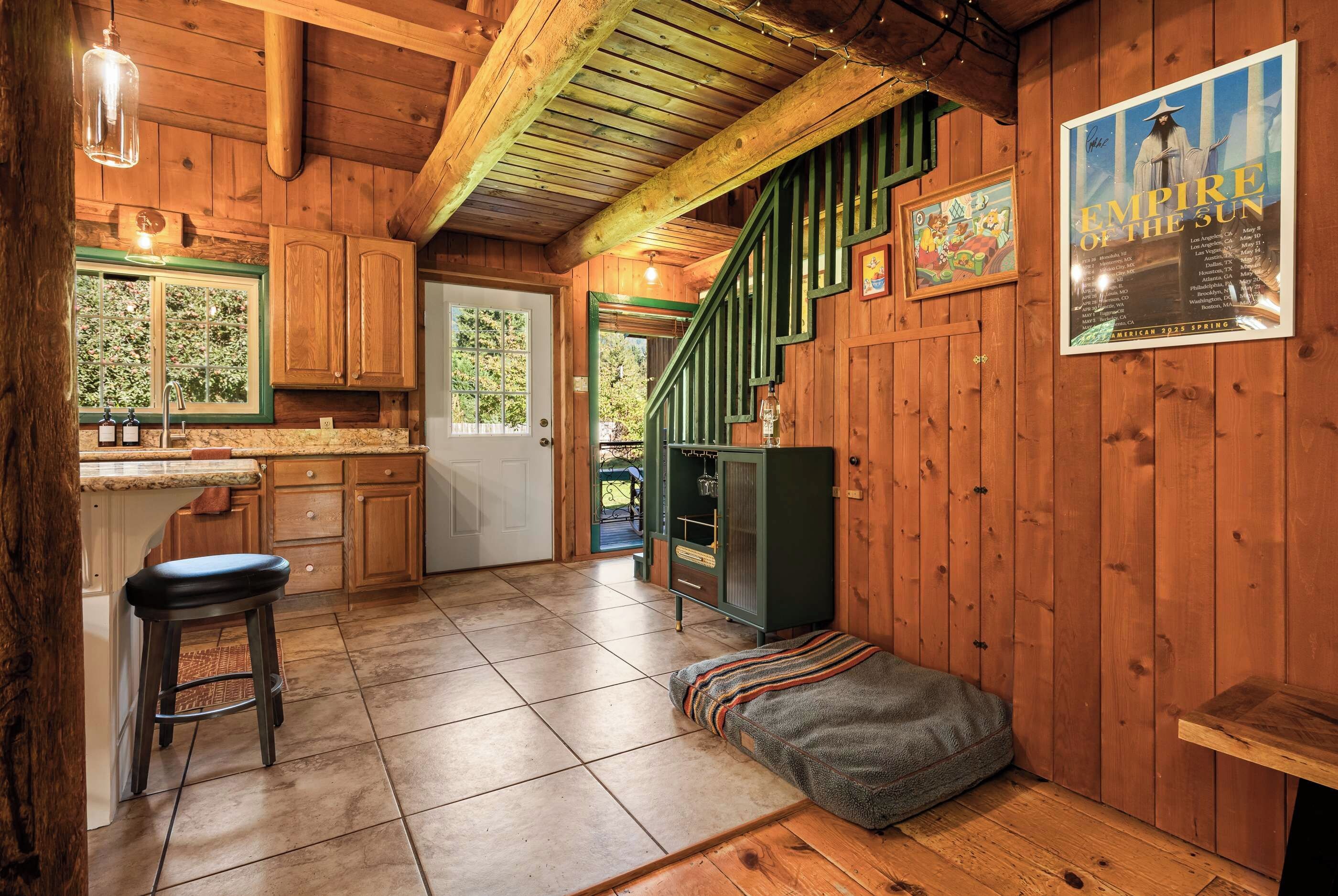 A rustic cabin interior with a kitchen, dining area, and a staircase leading to a loft.