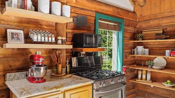A kitchen with wooden walls, a gas stove, a microwave, a red KitchenAid mixer, and various kitchen utensils and appliances.