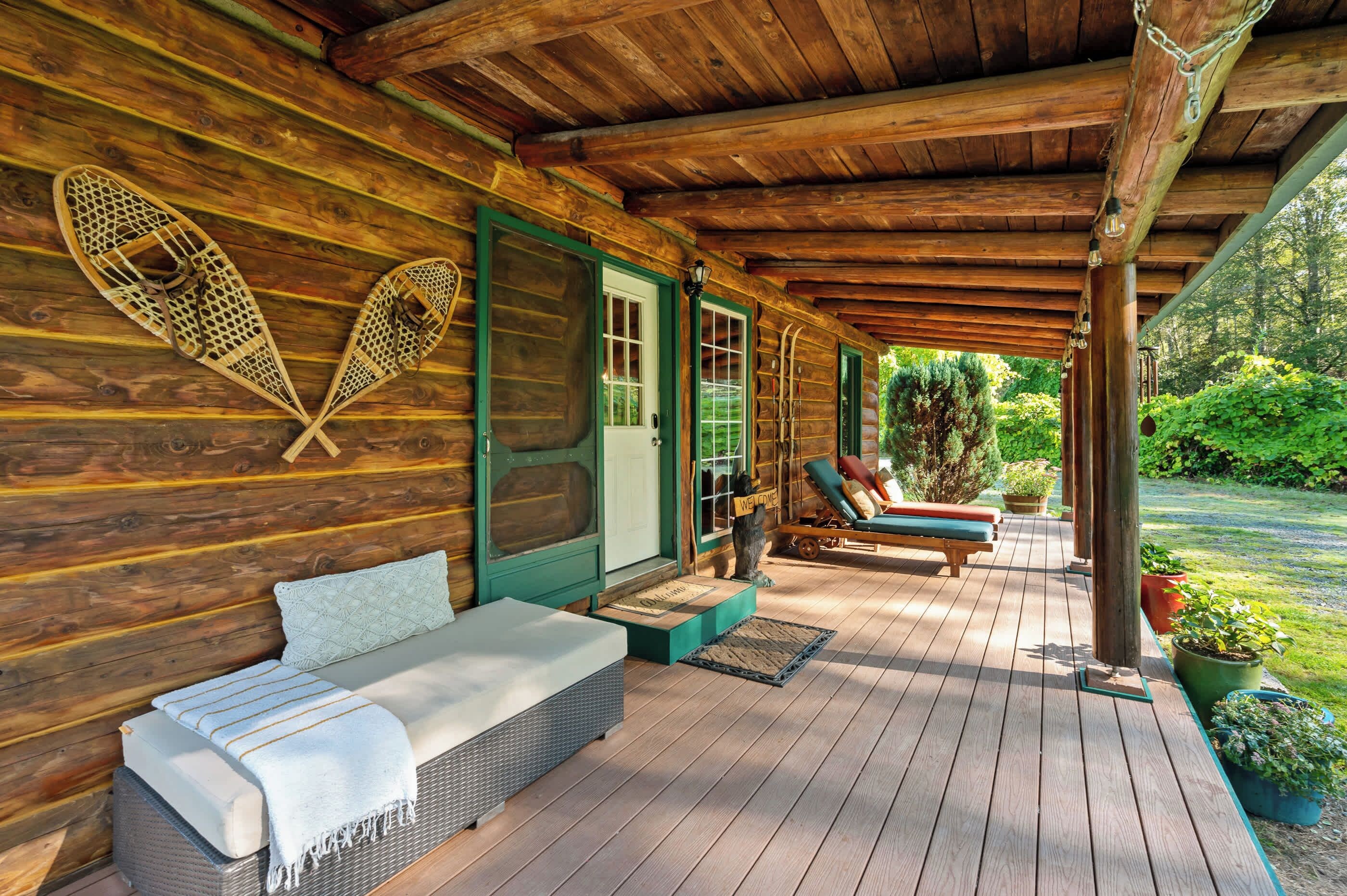 A wooden cabin with a covered porch, a bench, a welcome sign, and a row of skis.