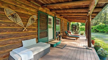 A wooden cabin with a covered porch, a bench, a welcome sign, and a row of skis.