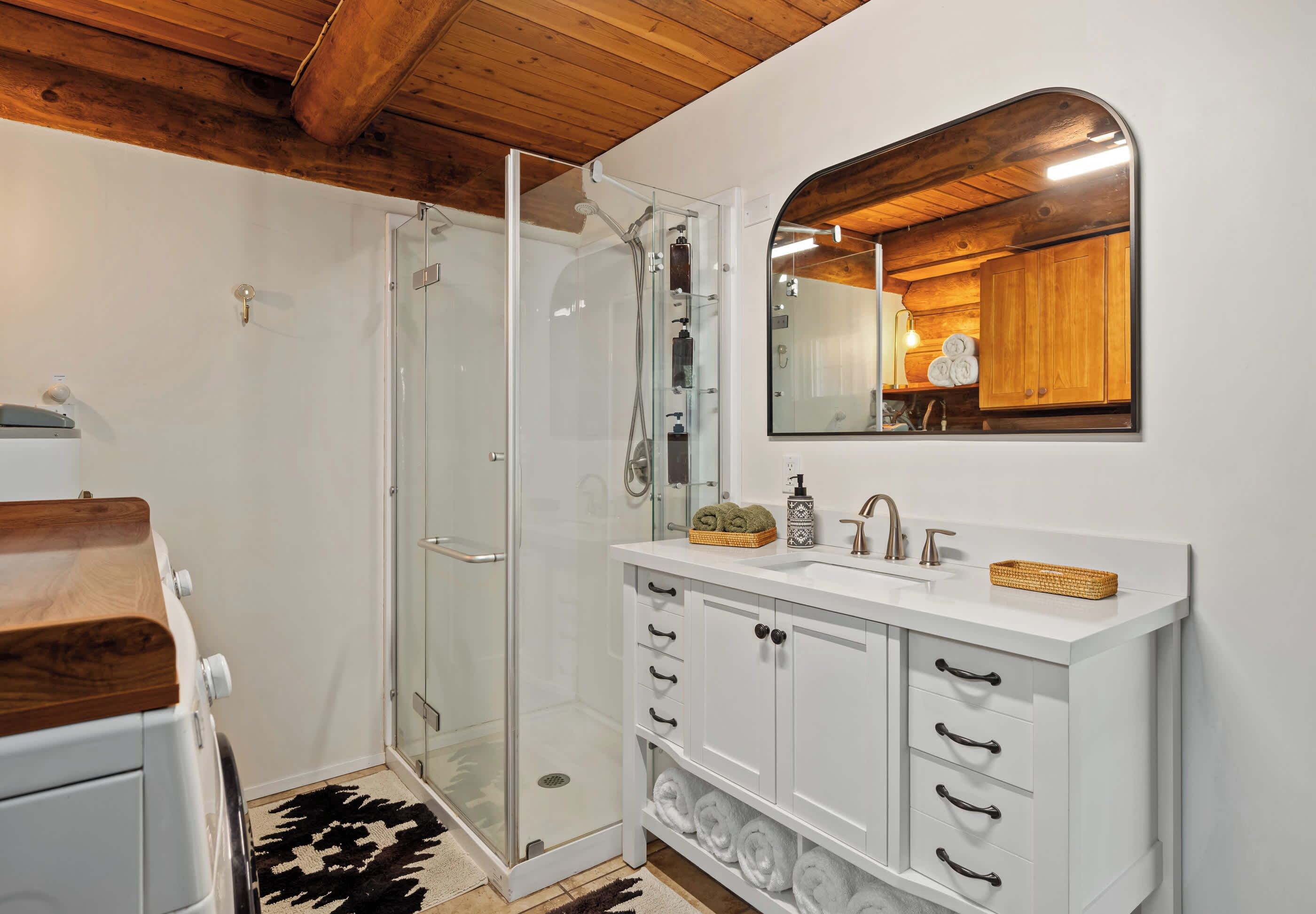 A modern bathroom with a glass shower enclosure, white cabinetry, and a wooden ceiling.