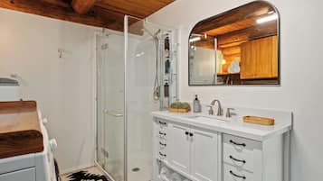 A modern bathroom with a glass shower enclosure, white cabinetry, and a wooden ceiling.