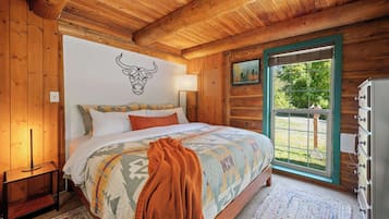Un dormitorio tipo cabaña de madera con cama, decoración de cabeza de toro en la pared, ventana con vistas y cómoda.