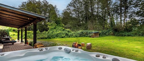 Un jacuzzi en un patio trasero con terraza de madera, sillas de descanso y una chimenea.