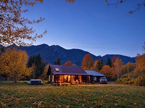 Una cabana amb un porxo i seients exteriors, envoltada per fullatge d'hivern i muntanyes al fons.