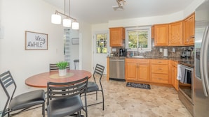 A modern kitchen with wooden cabinets, a stainless steel refrigerator, and a dining area with a round table and chairs. - Hershey's Hideaway: A Tranquil Retreat on the Hill (Palmyra)