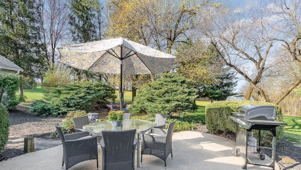 An outdoor patio with a glass table, wicker chairs, a patterned umbrella, and a barbecue grill. - Hershey's Hideaway: A Tranquil Retreat on the Hill (Palmyra)
