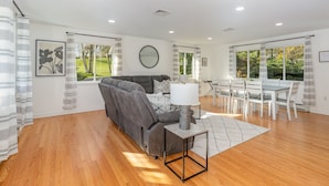 A spacious living room with a grey sofa, a dining table with chairs, and a large window with curtains. - Hershey's Hideaway: A Tranquil Retreat on the Hill (Palmyra)