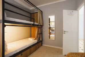 A bunk bed room with a mirror, a door, and a small wicker basket.