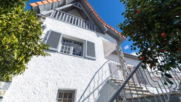 Un edificio blanco con techo de tejas rojas, un balcón y una escalera.