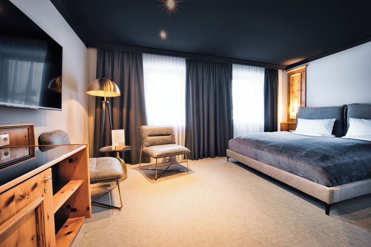 Ein modernes Hotelzimmer mit einem großen Bett, einem Schreibtisch mit Stuhl, einem Fernseher und einer Lampe.