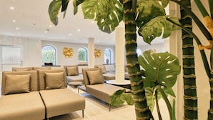 A modern lounge area with beige sofas and armchairs, large windows, and tropical plants. - Das Kronberg - Adults Only (Bodenmais)