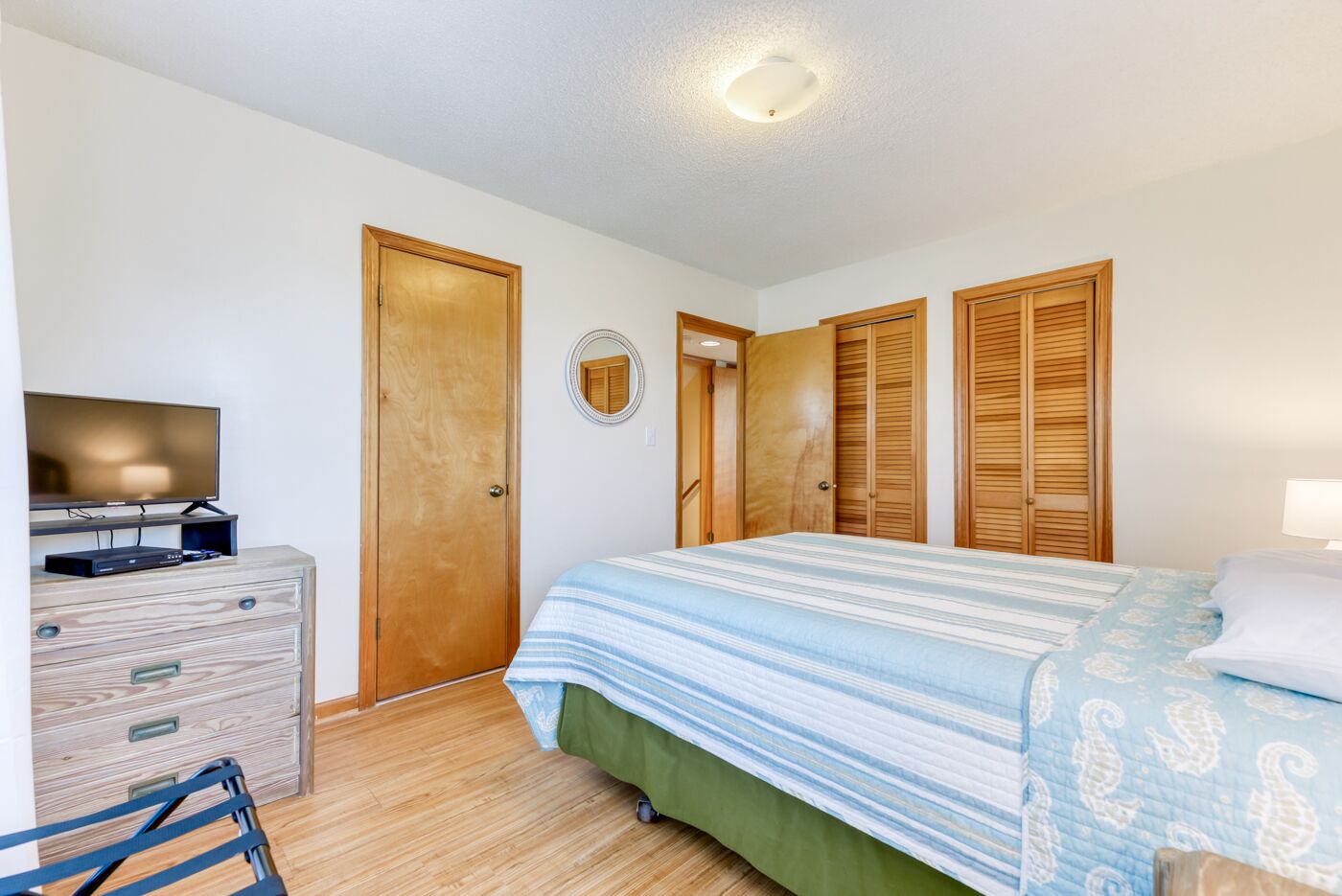 Une chambre à coucher avec un lit, une commode, un téléviseur et un placard.